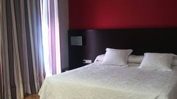 Quarto de hotel com uma cama grande, cabeceira escura e cortina listrada.