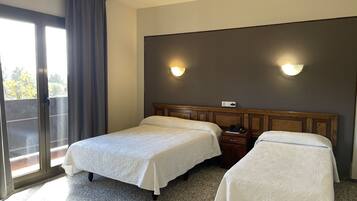 Una habitación de hotel con dos camas, un ventanal con cortinas y una lámpara fijada a la pared.