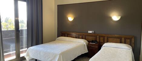 Una habitación de hotel con dos camas, un ventanal con cortinas y una lámpara fijada a la pared.