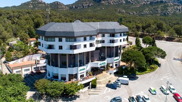 Un hotel con un patio central, varios pisos y montañas al fondo.