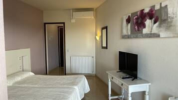 A hotel room with two beds, a TV on a small table, a radiator, and a painting on the wall.