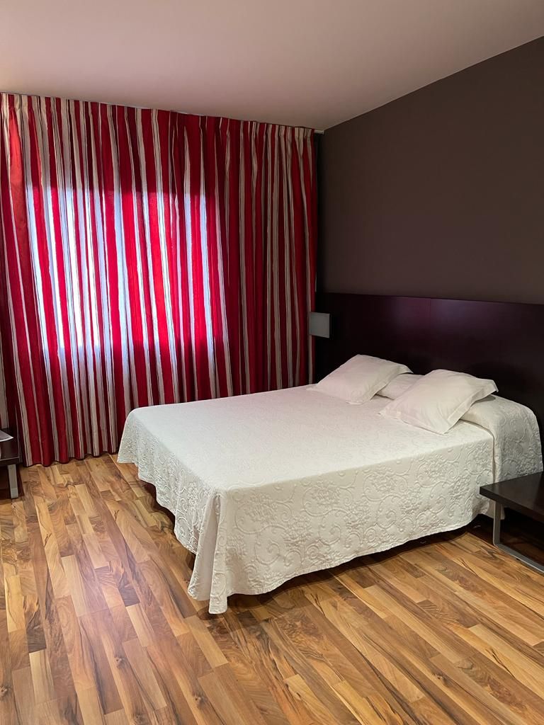 Ein Hotelzimmer mit einem Bett, Holzboden, einem Kopfteil und einem Vorhang mit vertikalen Streifen.