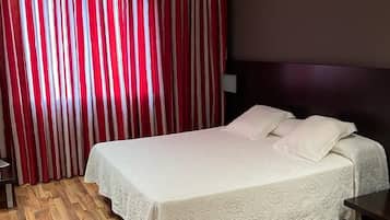 Une chambre d’hôtel avec un lit, un plancher en bois, une tête de lit et un rideau à rayures verticales.