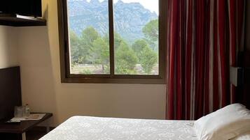 A hotel room with a large bed, a TV mounted on the wall, and a window with a mountain view.