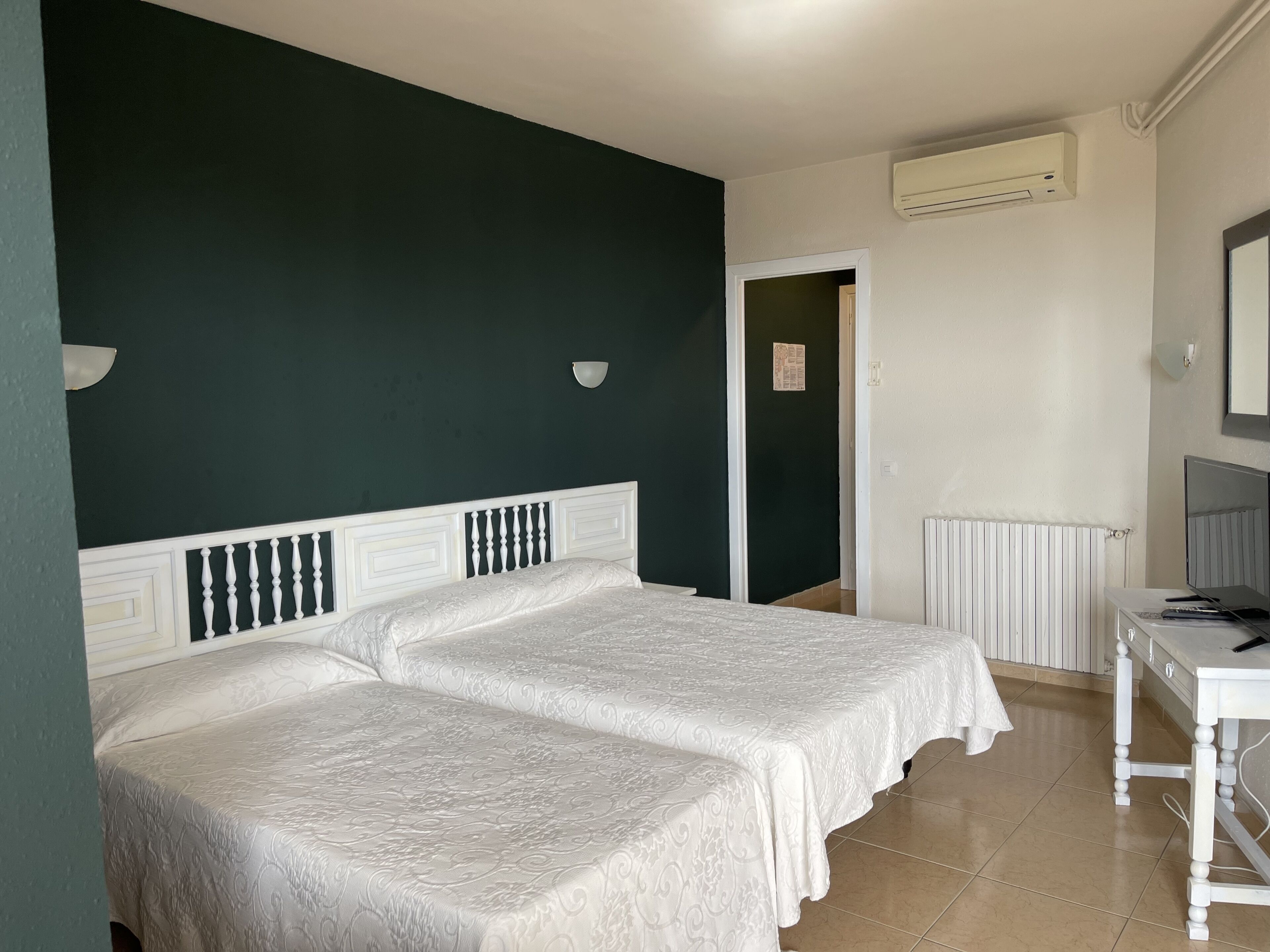 Una habitación con dos camas, un escritorio, una silla, un radiador y un equipo de aire acondicionado.