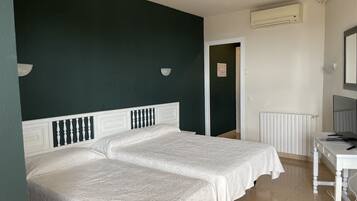 Een kamer met twee bedden, een bureau, een stoel, een radiator en een airconditioning.