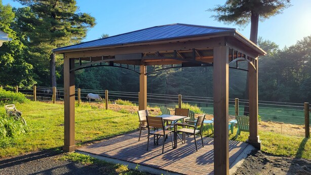 Un pabellón de madera con techo metálico, rodeado de un patio de ladrillo con mobiliario exterior.