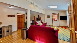 Un salón espacioso con un sofá rojo, suelo de madera, un televisor montado en la pared y un tragaluz.