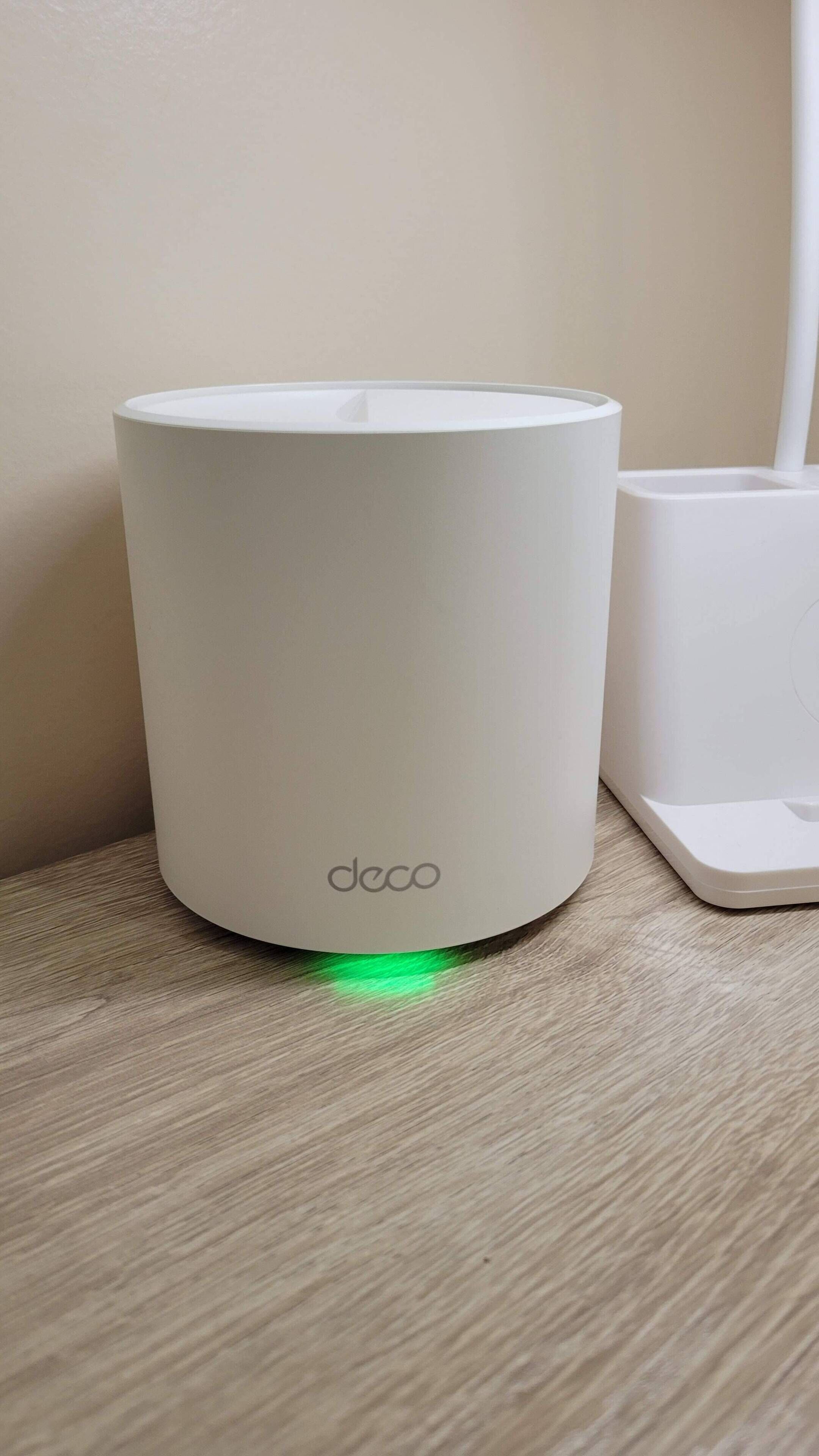 Un dispositivo cilíndrico blanco con el nombre de marca 'deco' en su base, sobre una superficie de madera junto a una taza blanca.