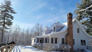 Una casa de dos pisos con chimenea de ladrillo, un porche y un patio cubierto de nieve.