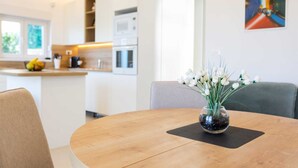 Una cocina moderna con armarios blancos, una mesa de comedor con un jarrón de flores blancas y un cuadro en la pared.