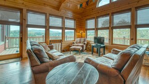 Relax in a spacious cabin with a comfortable seating area, large windows, and a balcony offering scenic views of the surrounding hills.