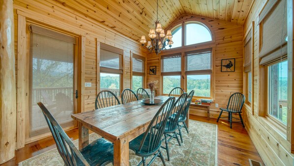 Cozy cabin dining area with a large round table and six classic chairs, surrounded by expansive forest views.