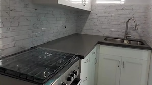 A kitchen with white cabinets, a gas stove, a sink, and a window with blinds.
