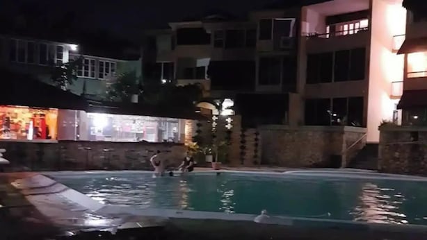 A nighttime view of a swimming pool area with a building in the background.