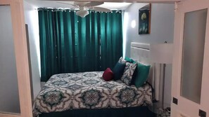 Une chambre à coucher avec une couvre-lit à motifs, une tête de lit blanche et un coussin rouge.