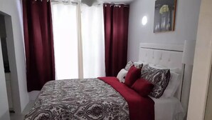 A neatly arranged bedroom with a patterned bedspread, red pillows, and a white headboard.