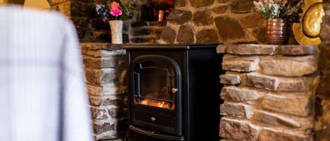 A stone fireplace with a black wood-burning stove, surrounded by stone walls and decorated with flowers.