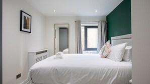 Une chambre à coucher bien rangée, avec un grand lit, une table de chevet, un miroir et une fenêtre avec des rideaux.