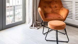 Une chambre moderne dotée d’une porte-fenêtre coulissante donnant sur un balcon, d’un grand mur végétal et d’un fauteuil orange, accompagné d’un pouf assorti.