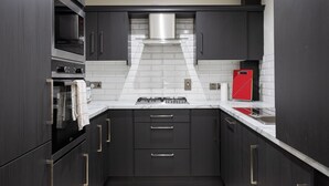 Une cuisine moderne avec des meubles de couleur sombre, une hotte de cuisine en acier inoxydable et un appareil électroménager rouge posé sur le plan de travail.