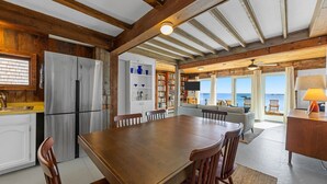 Une cuisine spacieuse avec des poutres en bois, une grande table à manger et une vue sur l’océan.
