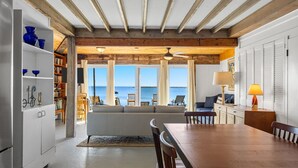 Un coin repas avec une table et des chaises en bois, un canapé blanc et une vue sur la mer grâce à de grandes fenêtres.