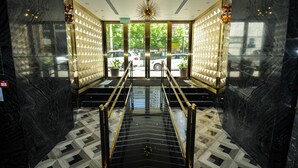Eine moderne Hotellobby mit einem geometrisch gemusterten Boden, einer zentralen Treppe und Blick auf geparkte Autos vor dem Haus.