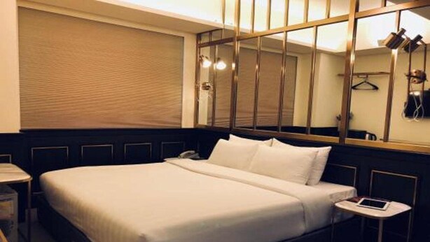 Ein Hotelzimmer mit einem großen Bett, einem Nachttisch mit Lampe, einem Spiegel und einem Kleiderhaken.