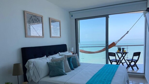 Una camera d'hotel con un letto grande, un balcone con un'amaca e vista sul mare.