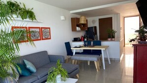 Un soggiorno moderno con divano, tavolino e poltrone, una zona pranzo con tavolo e sedie, e una cucina sullo sfondo.