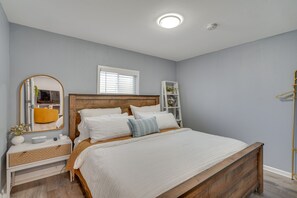 A bedroom with a wooden bed, white bedding, a bedside table with a lamp, a mirror, and a window with blinds. - Cozy Bay Area Vacation Rental with Patio (Hayward)