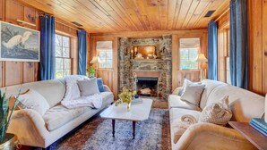 A cozy living room with wooden ceilings, a stone fireplace, two sofas, and a coffee table. - Historic Tennessee Vacation Rental on Homestead (Crossville)