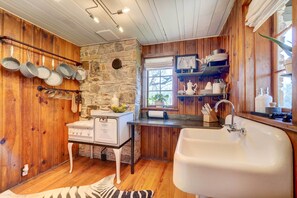 A rustic kitchen with wooden walls, a stone accent wall, and a large white sink. - Historic Tennessee Vacation Rental on Homestead (Crossville)