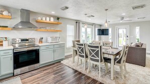 A modern kitchen with a stainless steel range, microwave, and oven. There is a dining area with a table and chairs, and a large window providing natural light. - Walk to Beach & Bay: Galveston Home w/ Pier Access (Galveston)