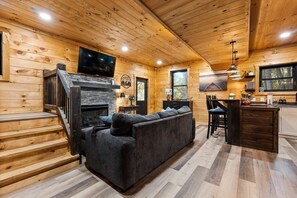 Un intérieur de chalet chaleureux, avec un revêtement mural en bois, une cheminée, un canapé et un coin cuisine.