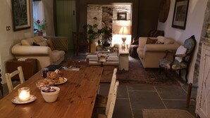 A cozy living room with a wooden dining table, two sofas, a stone fireplace, and a stone wall.
