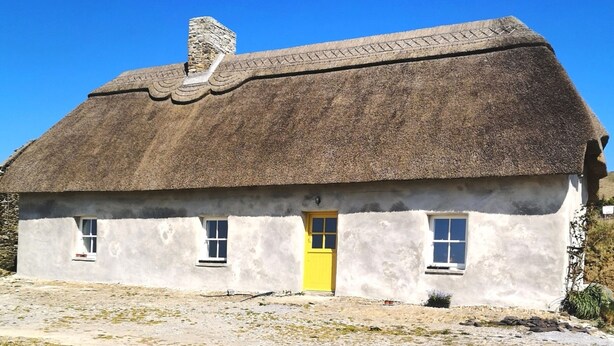 A traditional thatched-roof house with a single yellow door and two windows.