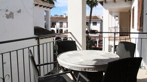 Un balcón con una mesa redonda y sillas, con vista a una zona residencial con palmeras y edificios.