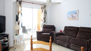 Una sala de estar con un sofá marrón, una mesa de comedor de madera y un televisor sobre un mueble.