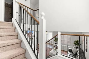 Staircase leads to an upper floor, flanked by a window and a white wall.