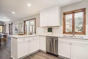 A modern kitchen with white cabinetry, a stainless steel dishwasher, and a window with a view of trees. - Blue Anchor Beach Home: Private Beach Access, Large Family Room, Spacious Accommodations (Holland)