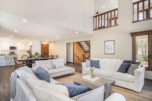 A spacious living area with a high ceiling, a staircase, and a kitchen in the background. - Blue Anchor Beach Home: Private Beach Access, Large Family Room, Spacious Accommodations (Holland)