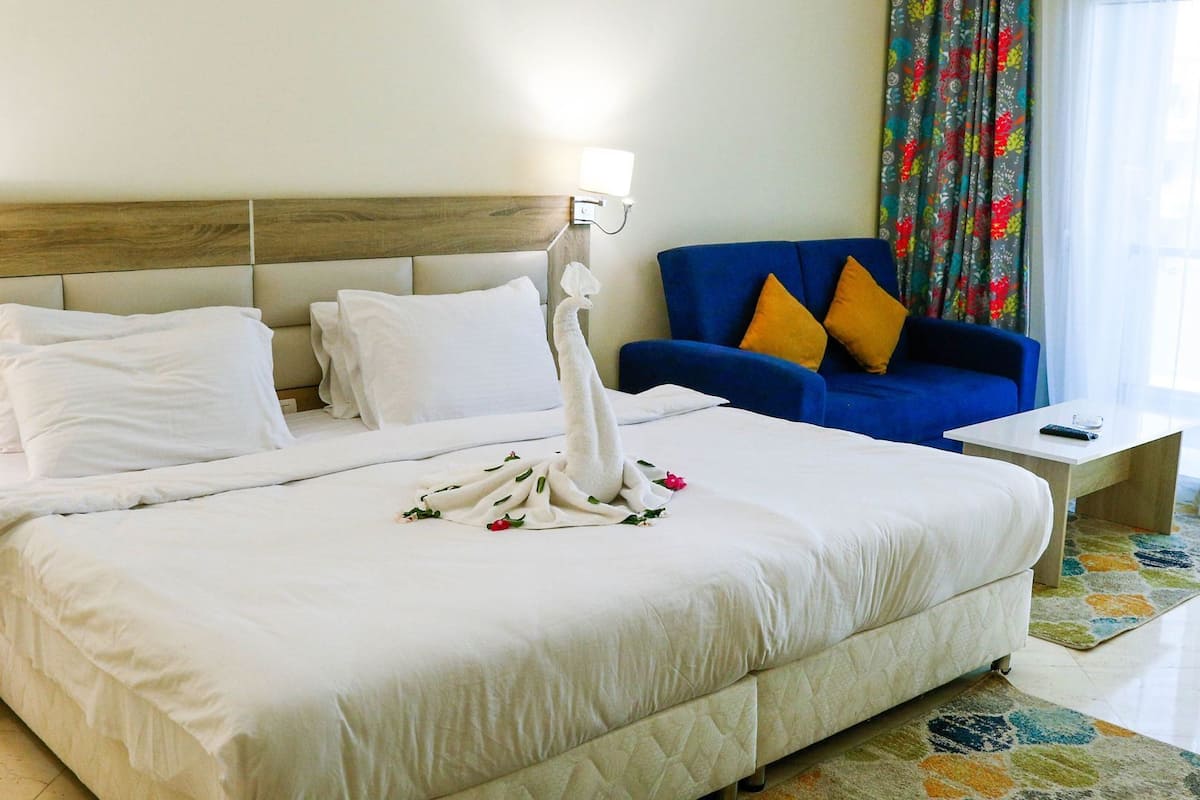 Ein Hotelzimmer mit einem großen Bett, einem blauen Sofa, einem kleinen Tisch und einem Fenster mit Vorhängen.