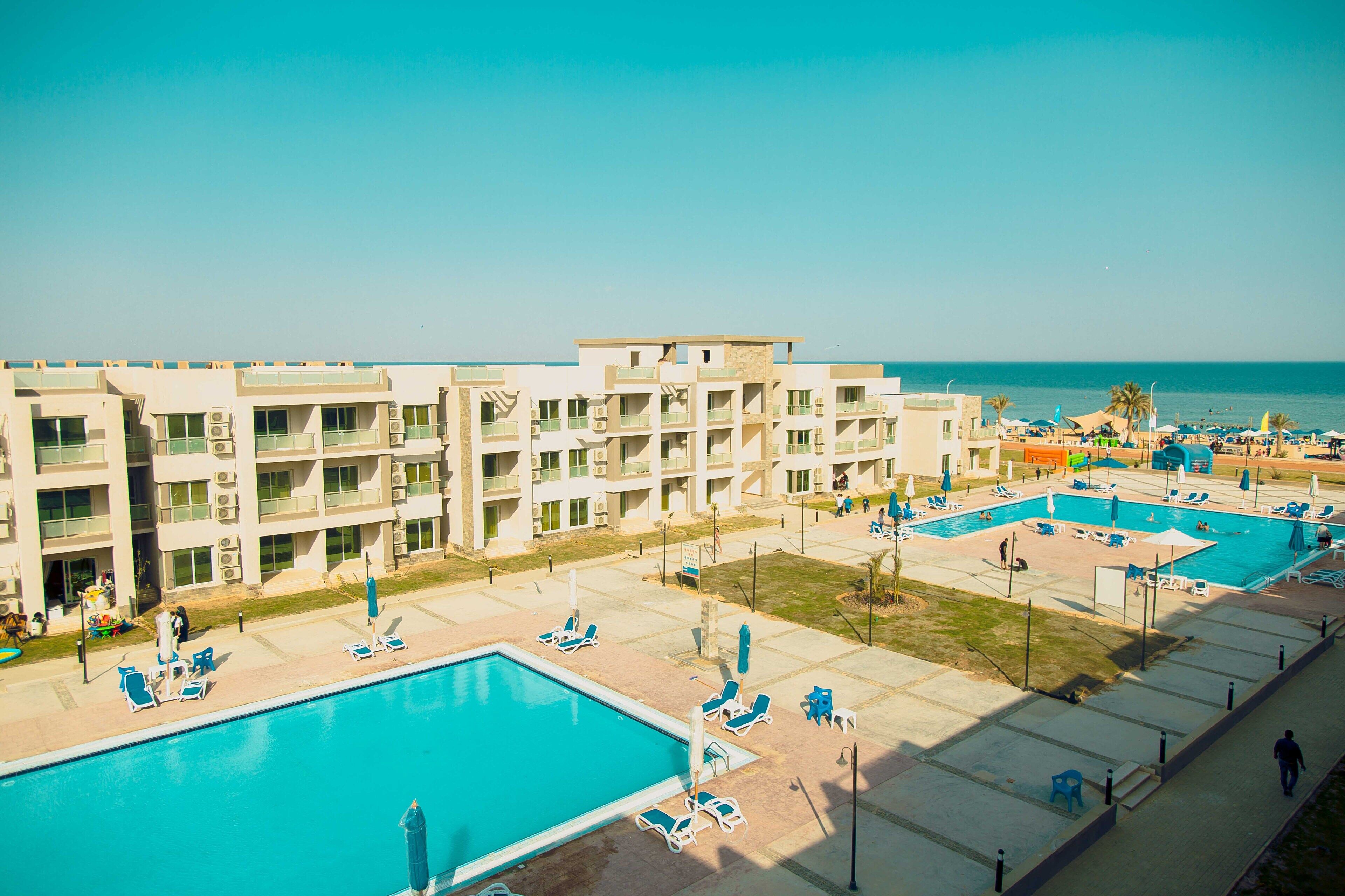 A hotel with multiple swimming pools, outdoor seating areas, and a view of the sea.