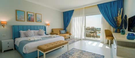 A modern hotel room with a large bed, a sofa, a desk, and a balcony with a pool view.