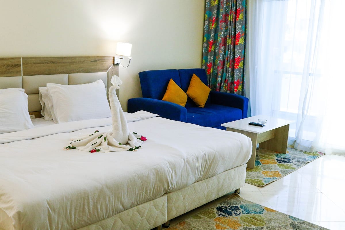 Ein Hotelzimmer mit Bett, blauem Sofa, kleinem Tisch und einem Fenster mit Vorhängen.
