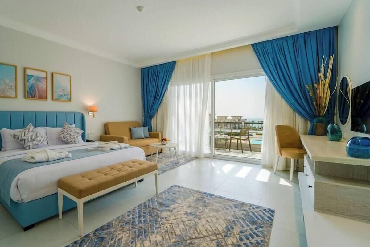 Ein Schlafzimmer mit Bett, Sitzbank, Nachttisch, Sofa, Schreibtisch und Blick ins Freie.