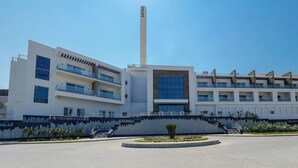 Un hotel moderno de varios pisos con balcones, una torre central y un patio ajardinado.