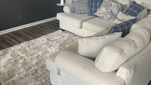 Ein modernes Wohnzimmer mit einer grauen Sofagarnitur, einem weißen Teppich und einem an der Wand montierten Flachbildfernseher.